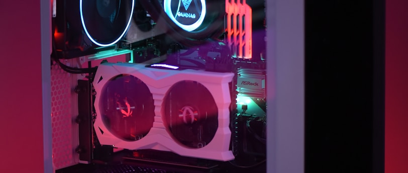 A gaming computer with visible internal components such as cooling fans and LED lights in a transparent case. The lighting emits a colorful glow with shades of purple, blue, and red.