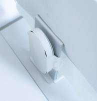 A white, sleek, vertical gaming console placed beside a large, slim monitor. The setting exudes minimalism with a focus on modern technology design.